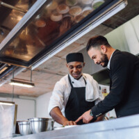 Restaurant manager discussing with chef in kitchen.