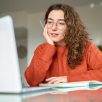 Young woman student using laptop elearning or remote working at home office using laptop computer watching webinar, learning web course, studying online sitting at table, writing notes.