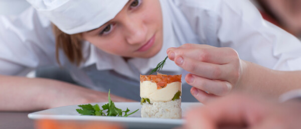 A close up shot of a young female trainee chef looking at desert while garnishing in a kitchen.