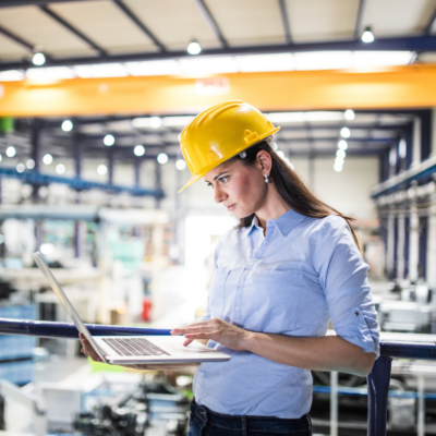 Female project manager standing in modern industrial factory using a laptop