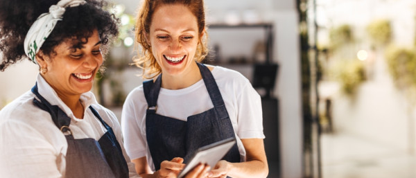 Happy female employees using a mobile app on a tablet to manage the daily operations of their restaurant. Women working together to ensure that customers receive the best hospitality service.